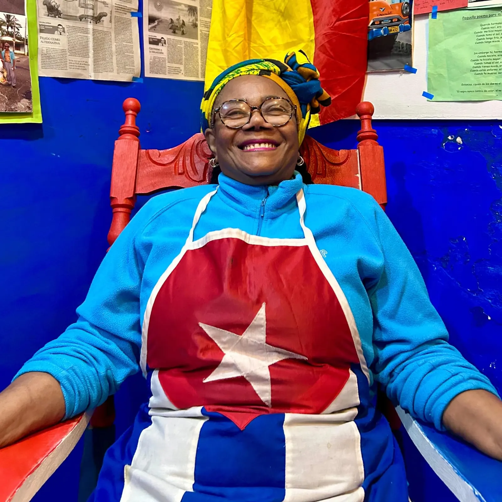 Mamá Nancy sonriendo en su silla roja con camiseta de la bandera cubana